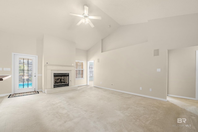 unfurnished living room with a tiled fireplace, high vaulted ceiling, a ceiling fan, and light carpet