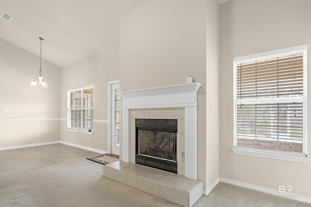 unfurnished living room with a wealth of natural light, carpet flooring, a tile fireplace, and a chandelier