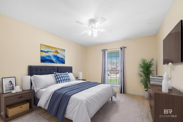 bedroom featuring light carpet, ceiling fan, a textured ceiling, and baseboards