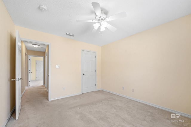 unfurnished bedroom featuring visible vents, baseboards, light carpet, a textured ceiling, and a ceiling fan