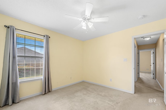 empty room featuring a textured ceiling, a ceiling fan, baseboards, and light carpet