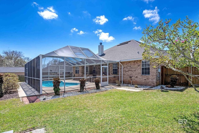 rear view of house with brick siding, a fenced in pool, fence, a chimney, and a yard