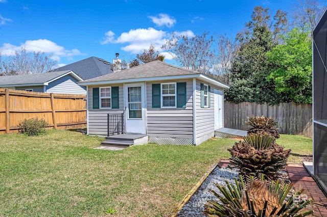 rear view of property featuring a lawn, an outdoor structure, a fenced backyard, and roof with shingles