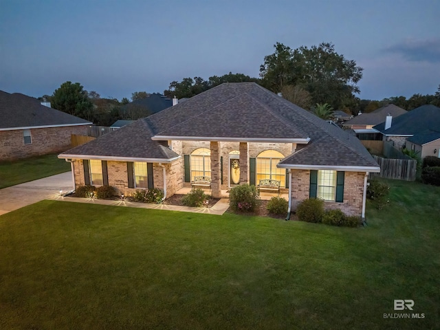 view of front facade with a front yard, fence, brick siding, and roof with shingles