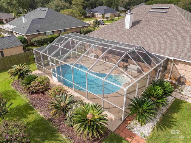 outdoor pool with glass enclosure, a patio, a yard, and fence