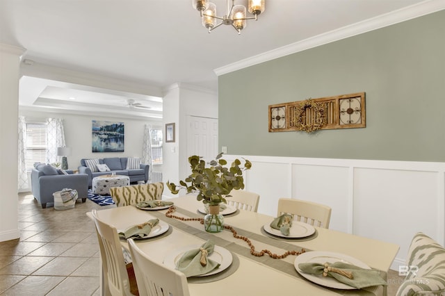 dining space with ceiling fan with notable chandelier, ornamental molding, a raised ceiling, and light tile patterned flooring