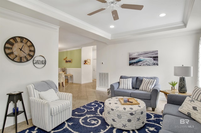 living room with ceiling fan, ornamental molding, a tray ceiling, and light tile patterned floors