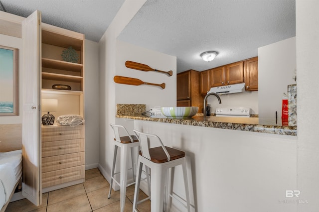 kitchen featuring a kitchen breakfast bar, kitchen peninsula, light stone countertops, light tile patterned flooring, and a textured ceiling