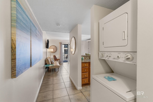 laundry room with stacked washer / drying machine, a textured ceiling, and light tile patterned floors