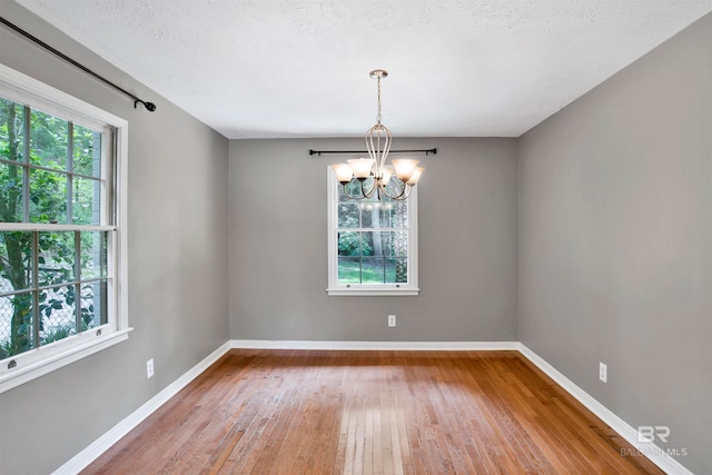 empty room featuring hardwood / wood-style floors, a healthy amount of sunlight, and an inviting chandelier