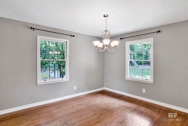 unfurnished room with wood-type flooring and an inviting chandelier