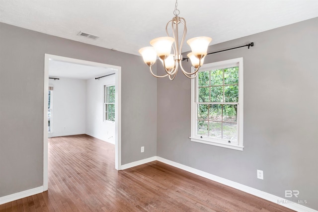 spare room featuring plenty of natural light, a notable chandelier, and hardwood / wood-style flooring