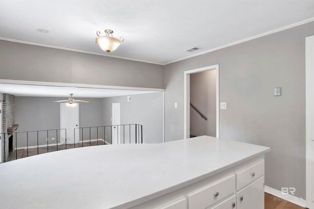 kitchen with wood-type flooring, ornamental molding, ceiling fan, and white cabinetry