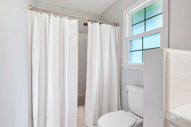 bathroom with shower / tub combo, toilet, and a wealth of natural light