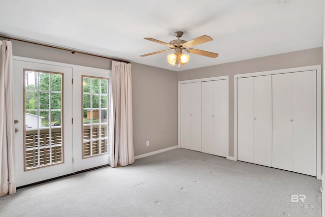 unfurnished bedroom featuring light colored carpet, ceiling fan, access to exterior, and multiple closets