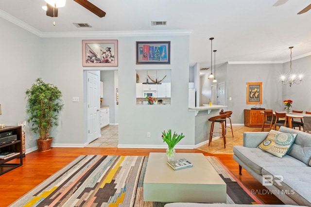 living room featuring ornamental molding, light hardwood / wood-style flooring, and ceiling fan with notable chandelier