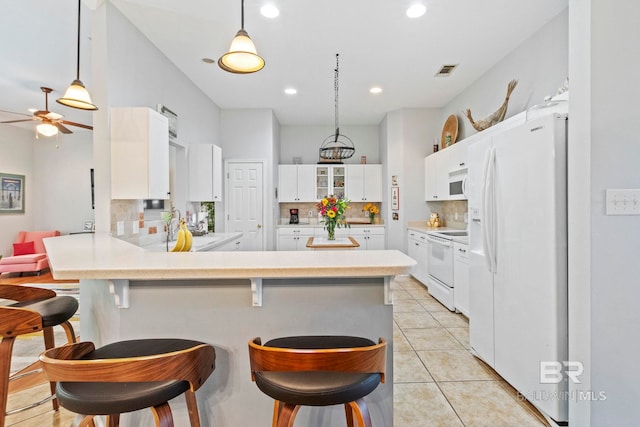 kitchen featuring decorative backsplash, white cabinets, a breakfast bar area, light tile patterned floors, and white appliances