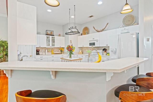 kitchen featuring a breakfast bar, white cabinets, pendant lighting, and white appliances