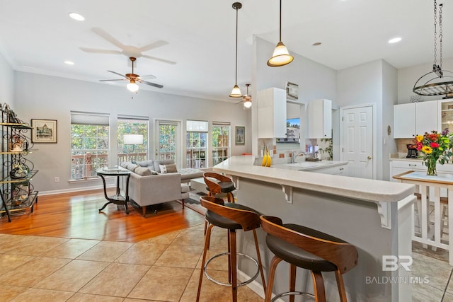 kitchen featuring a breakfast bar area, kitchen peninsula, decorative light fixtures, light wood-type flooring, and white cabinets