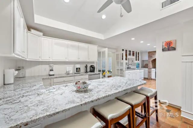 kitchen featuring white cabinets, a kitchen breakfast bar, kitchen peninsula, and light stone countertops