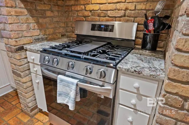 room details with stainless steel gas range oven, light stone counters, and white cabinetry