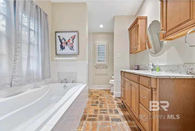 bathroom featuring vanity, a relaxing tiled tub, toilet, and a wealth of natural light