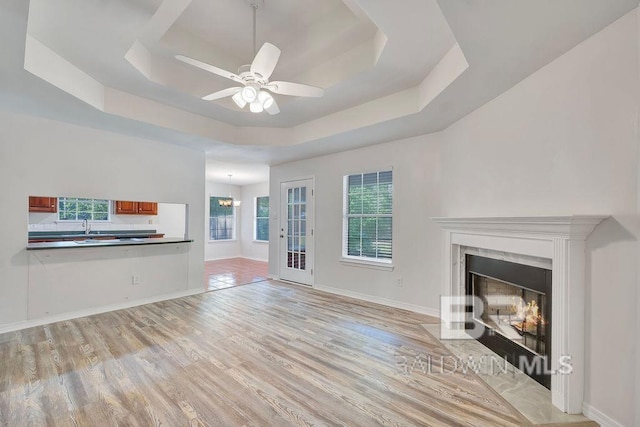 31246 Shambo Rd, Spanish Fort, AL 36527 - unfurnished living room with a tray ceiling, light wood-type flooring, a premium fireplace, a ceiling fan, and a chandelier