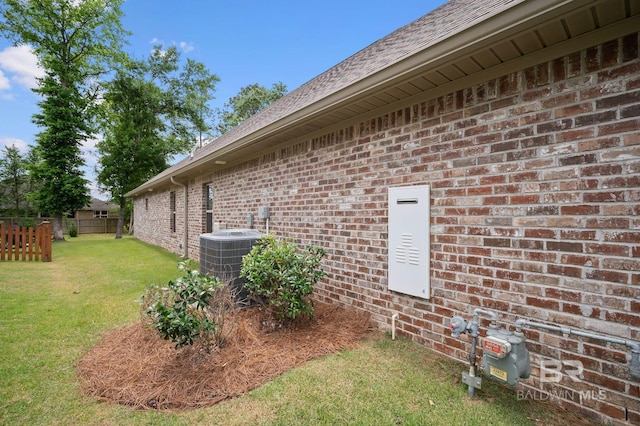 view of property exterior with central air condition unit, brick siding, fence, a yard, and a shingled roof