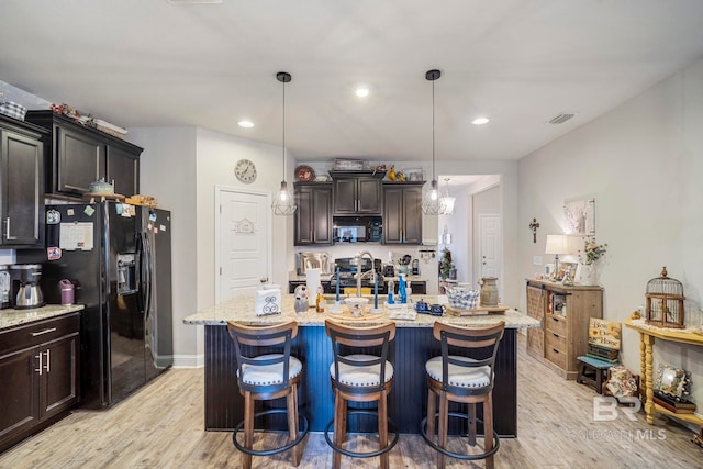 kitchen with black appliances, dark brown cabinetry, light wood-type flooring, and an island with sink