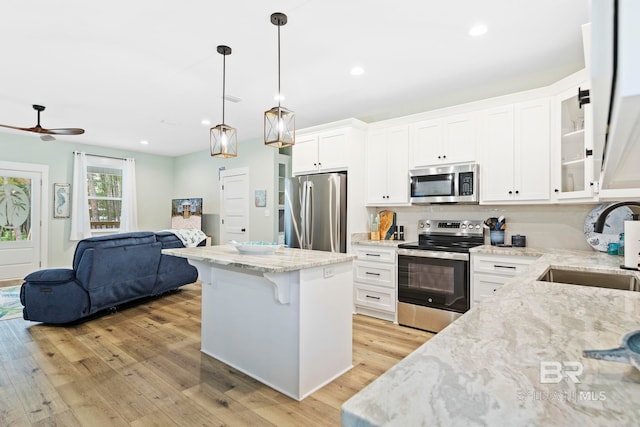 kitchen featuring stainless steel appliances, white cabinetry, pendant lighting, and light hardwood / wood-style flooring