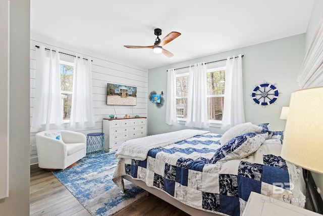 bedroom with multiple windows, light wood-type flooring, wooden walls, and ceiling fan