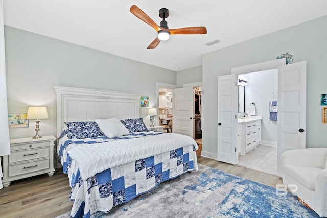 bedroom with ceiling fan, ensuite bath, a spacious closet, and hardwood / wood-style flooring