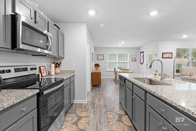 kitchen featuring sink, gray cabinets, light wood-type flooring, appliances with stainless steel finishes, and light stone counters