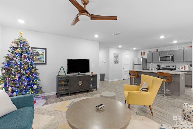 living room featuring ceiling fan, sink, and light hardwood / wood-style flooring