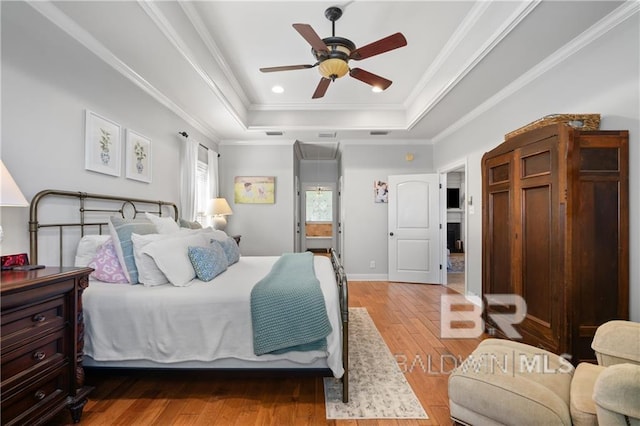 bedroom with hardwood / wood-style flooring, ceiling fan, crown molding, and a tray ceiling