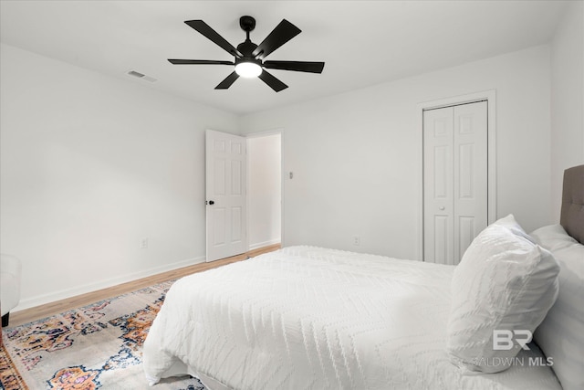 bedroom with ceiling fan, visible vents, wood finished floors, baseboards, and a closet