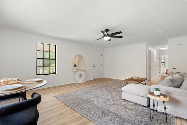 living area featuring crown molding, light wood-style flooring, a ceiling fan, baseboards, and visible vents
