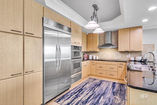 kitchen featuring light brown cabinetry, appliances with stainless steel finishes, sink, hanging light fixtures, and wall chimney exhaust hood