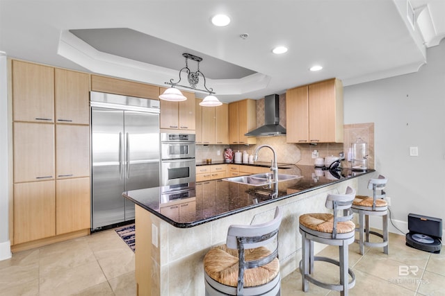 kitchen featuring appliances with stainless steel finishes, wall chimney exhaust hood, hanging light fixtures, and kitchen peninsula