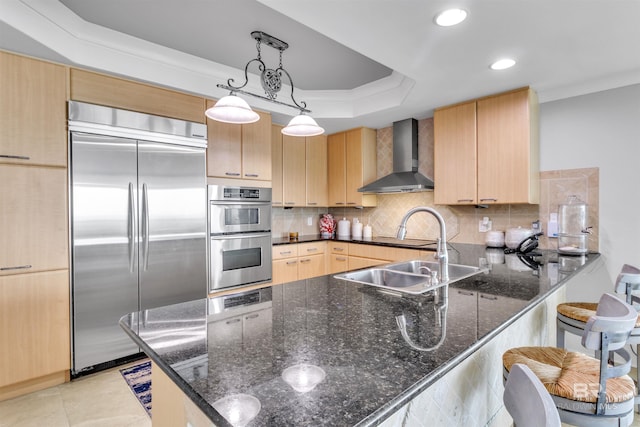 kitchen with hanging light fixtures, wall chimney range hood, stainless steel appliances, and dark stone countertops