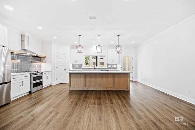 kitchen featuring white cabinets, wall chimney exhaust hood, stainless steel appliances, tasteful backsplash, and a large island