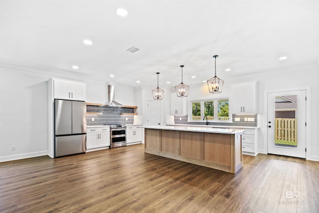 kitchen with white cabinetry, appliances with stainless steel finishes, tasteful backsplash, wall chimney range hood, and a kitchen island