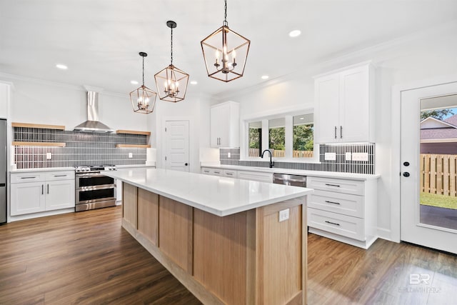 kitchen featuring wall chimney range hood, white cabinets, stainless steel appliances, and a kitchen island