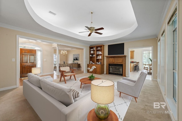 living room featuring ceiling fan with notable chandelier, a tray ceiling, crown molding, and light colored carpet