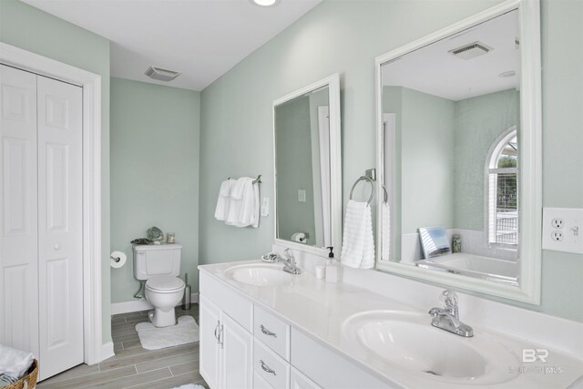 bathroom with toilet, a washtub, and dual bowl vanity