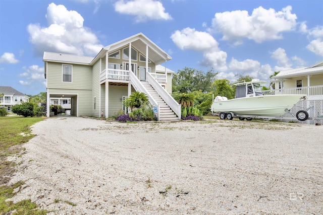 coastal home featuring stairway, a porch, metal roof, a carport, and driveway