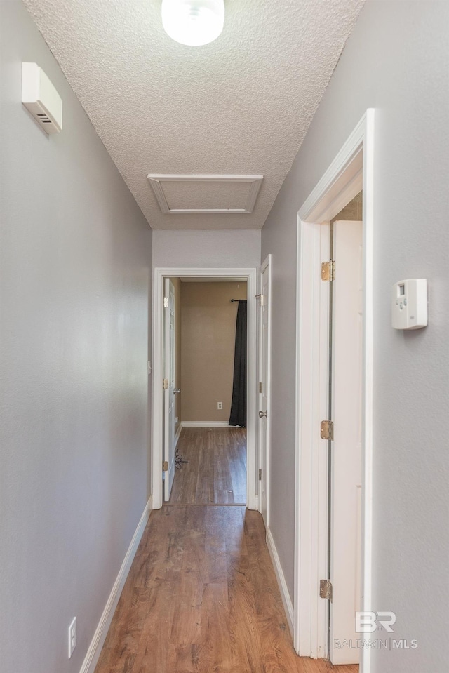 corridor with baseboards, a textured ceiling, attic access, and wood finished floors