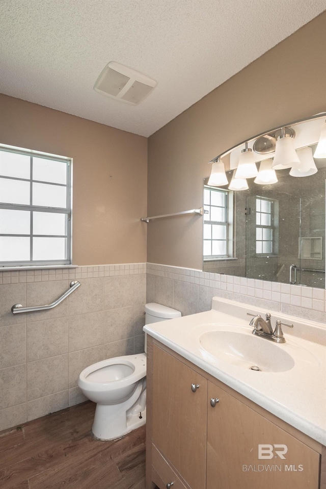 full bath with toilet, tile walls, vanity, wood finished floors, and a stall shower