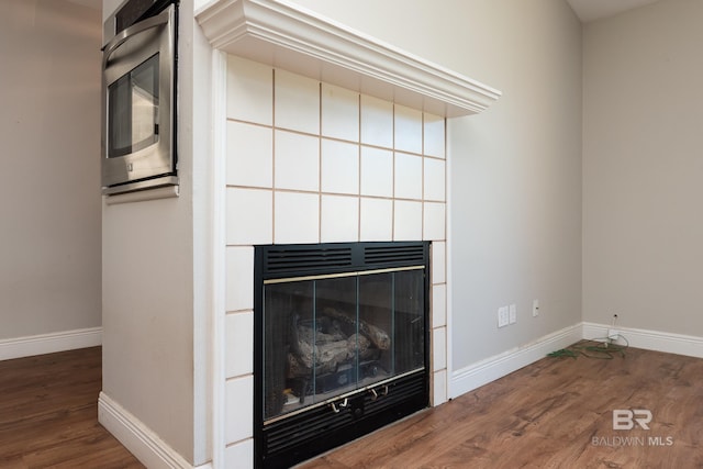 details featuring a tiled fireplace, baseboards, and wood finished floors