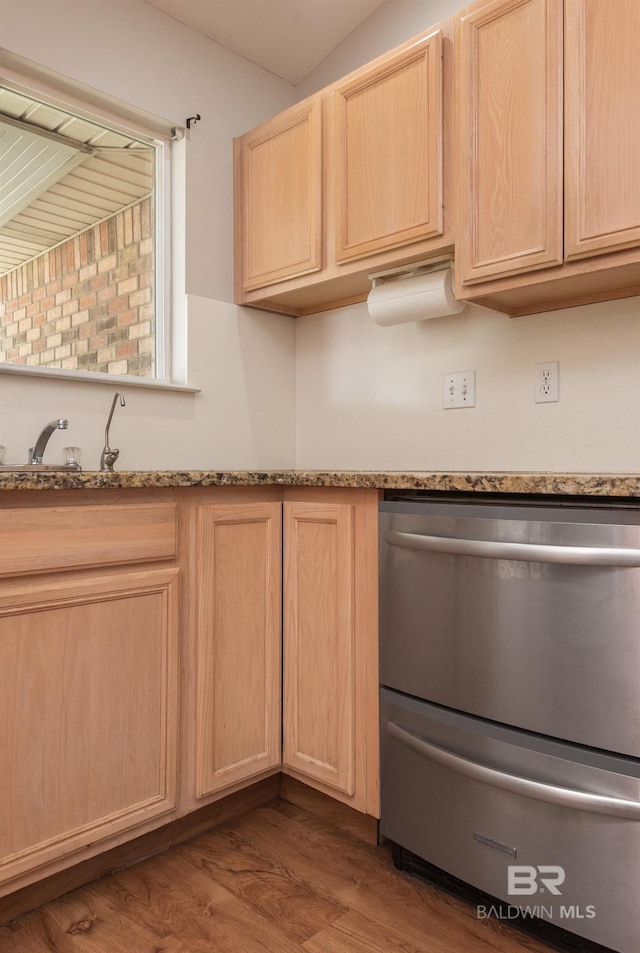 kitchen featuring stainless steel dishwasher, light stone counters, light brown cabinetry, and wood finished floors